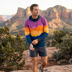 Man in colorful running hoodie and shorts standing in a desert landscape with mountains in the background