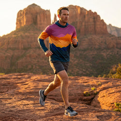 Man wearing a lightweight hoodie running on a rocky trail with red rock formations in the background