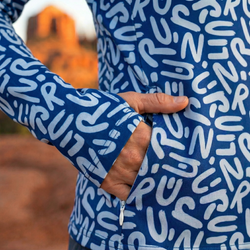 Person wearing a blue jacket with white text pattern showing a zippered side pocket, blurred outdoor background