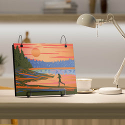 Desk with a colorful bibfolio featuring a sunset and running person design, next to a lamp and cup.