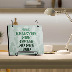 Desk Bibfolio with a motivational graphic reading 'She believed she could so she did' and a lamp.