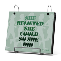 Bibfolio on a stand with 'She believed she could so she did' text on a light green background