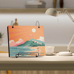 Desk bibfolio with a scenic design on a desk next to a lamp and cup.