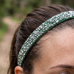Close-up of a person wearing a green headband with rhinestones against a blurred natural background.