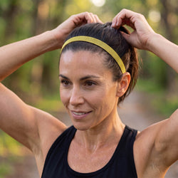 Woman adjusting a yellow headband outdoors with greenery in the background