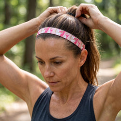 Woman adjusting a pink headband outdoors with greenery in the background