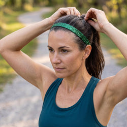 Woman adjusting her hair with a green headband outdoors