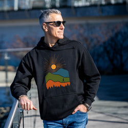 Man wearing a black hoodie with a colorful mountain design outdoors.