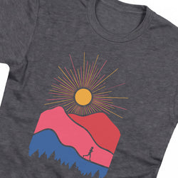 A close-up of a dark heather gray t-shirt featuring a colorful graphic print of a sunburst over pink and blue mountains with a small runner silhouette.