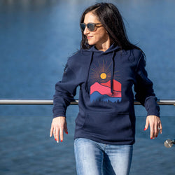 Woman wearing a navy hoodie with a mountain design by a body of water