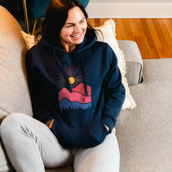 Woman wearing a navy hoodie with a colorful mounain design, sitting on a couch.