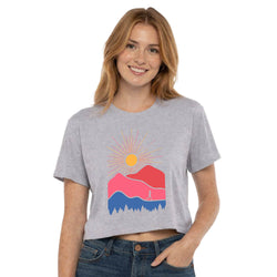 Woman wearing a gray t-shirt with a colorful mountain and sun graphic design on a white background