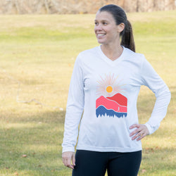 Woman wearing a white long-sleeve shirt with a mountain and sun design outdoors