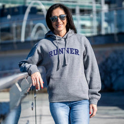Woman wearing a gray hoodie with 'RUNNER' printed on it, standing outdoors.