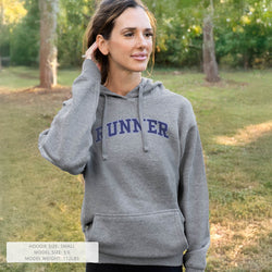 Woman wearing a gray hoodie with 'RUNNER' printed on it, standing outdoors.
