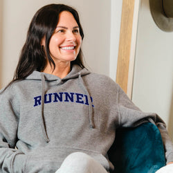 Woman wearing a gray hoodie with 'RUNNER' printed on it, sitting indoors.
