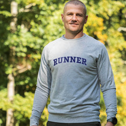 Man wearing a gray sweatshirt with 'RUNNER' printed on it, standing outdoors with greenery in the background.