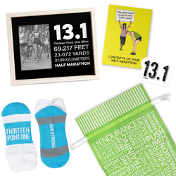 Collection of half marathon-themed items including socks, a photo frame, a greeting card and a 13.1 sticker on a white background. Includes a green motivational word gift bag.