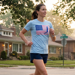 Woman running on a street wearing a light blue t-shirt with an American flag design.
