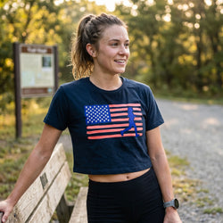 Woman wearing a t-shirt with an American flag and running silhouette design, standing outdoors.