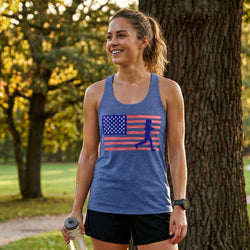 Woman wearing a blue tank top with an American flag and running woman graphic, standing outdoors.