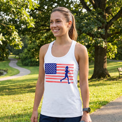 Woman wearing a white tank top with an American flag and running woman graphic in a park.