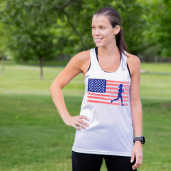 Woman wearing a tank top with an American flag and running woman graphic in a park.