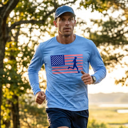 Man running outdoors wearing a blue long-sleeve shirt with an American flag and runner graphic.