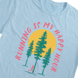 A close-up of a light blue t-shirt featuring a graphic print of three green pine trees in front of a yellow sun, with the pink text 'RUNNING IS MY HAPPY HOUR' arched around them.