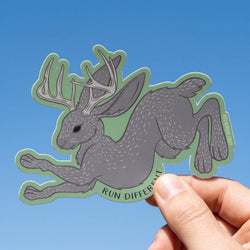 Sticker of a jackalope with antlers held by a hand against a blue sky background