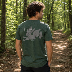 A man standing on a forest path, viewed from behind, wearing a dark green heathered t-shirt with a large gray graphic of a running jackalope on the back.