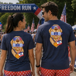 Two people standing outdoors at a race, shown from the back wearing matching navy blue t-shirts with a large patriotic dog graphic on the back and red star-patterned shorts.
