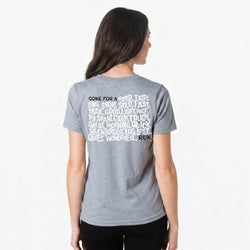 Person wearing a gray t-shirt with running text on the back, standing against a white background