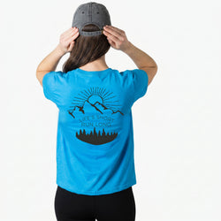 Person wearing a blue t-shirt with a mountain graphic and 'Life's Short Run Long' text, holding a cap.