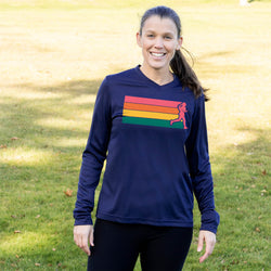 A woman standing outdoors on a grassy lawn wearing a navy long-sleeve athletic shirt with a rainbow-striped chest graphic and a pink silhouette of a running person, paired with black leggings.