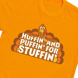 Bright orange t-shirt featuring a cartoon turkey graphic with the text 'HUFFIN' AND PUFFIN' FOR STUFFIN'' in bold white letters with a brown outline.