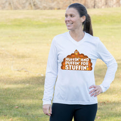 A woman wearing a white long-sleeve V-neck t-shirt with a cartoon pumpkin graphic that reads 'HUFFIN' AND PUFFIN' FOR STUFFIN'' in orange and brown, standing in an outdoor grassy field.