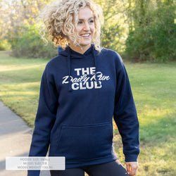 A woman wearing a navy blue hoodie with 'THE Daily Run CLUB' printed in white across the chest, standing outdoors on a grassy path with trees in the background. A text overlay at the bottom left provides sizing and weight information.