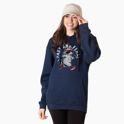 A woman wearing a navy blue hoodie with a graphic of a raccoon in sunglasses and the words 'FAST AND FERAL' on the front, paired with a beige bucket hat and black pants, against a plain white background.