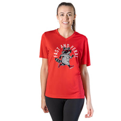 A woman modeling a red short-sleeve V-neck athletic T-shirt with a large front graphic of a raccoon running under the words 'FAST AND FERAL'. She is wearing black leggings against a plain white studio background.