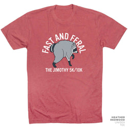 A heathered red crewneck t-shirt featuring a graphic of a raccoon walking with the text 'FAST AND FERAL' above and 'THE JIMOTHY 5K/10K' below. A small brand label in the bottom right corner reads 'HEATHER REDWOOD UNISEX TEE'.