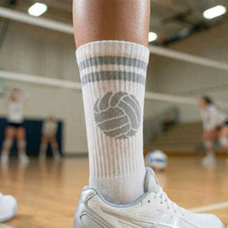 Person wearing a white sock with a volleyball design on a sports court.