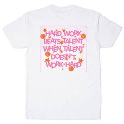A white short-sleeve t-shirt with a retro-style graphic on the front. The graphic features the text 'HARD WORK BEATS TALENT WHEN TALENT DOESN'T WORK HARD' in pink letters, surrounded by orange starbursts, volleyballs, and a pink grid background.