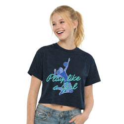 A smiling young woman wearing a cropped navy T-shirt with a blue volleyball graphic and the text 'Play like a Girl' in teal, paired with light-wash jeans, against a plain white background.