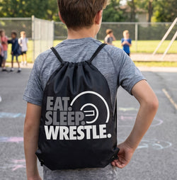 Person wearing a black drawstring bag with 'EAT. SLEEP. WRESTLE.' text on a sports field.