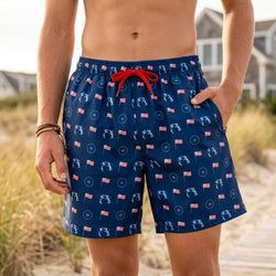 Person wearing navy blue swim shorts with a wrestling and usa flag pattern on a beach.