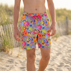 Person wearing colorful tropical-themed wrestling swim trunks on a sandy beach.