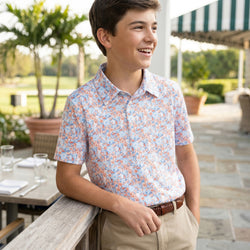 Young man in a wrestling patterned polo shirt standing outdoors near a table with a striped awning in the background.
