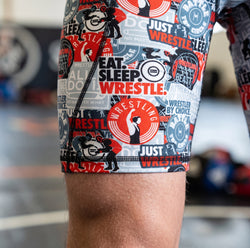 Wrestling-themed athletic shorts with various graphics and text worn by a person.